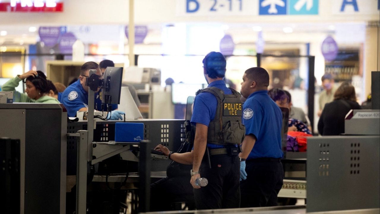 TSA officers working at an airport security checkpoint with travelers in line, news photography style
