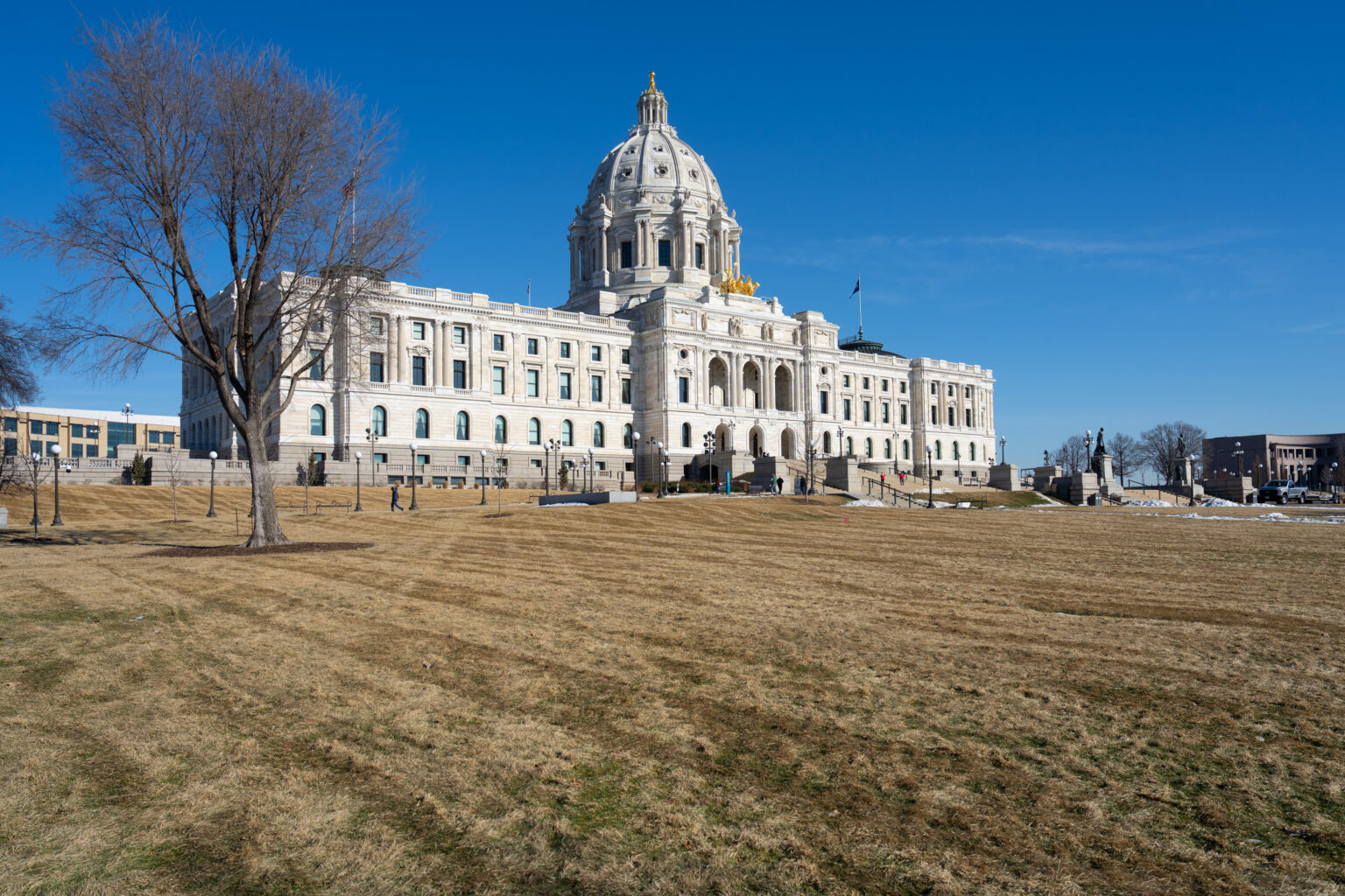 The Minnesota State Capitol in Saint Paul with legislators and staff walking near the entrance during an active legislative session day, news photography style