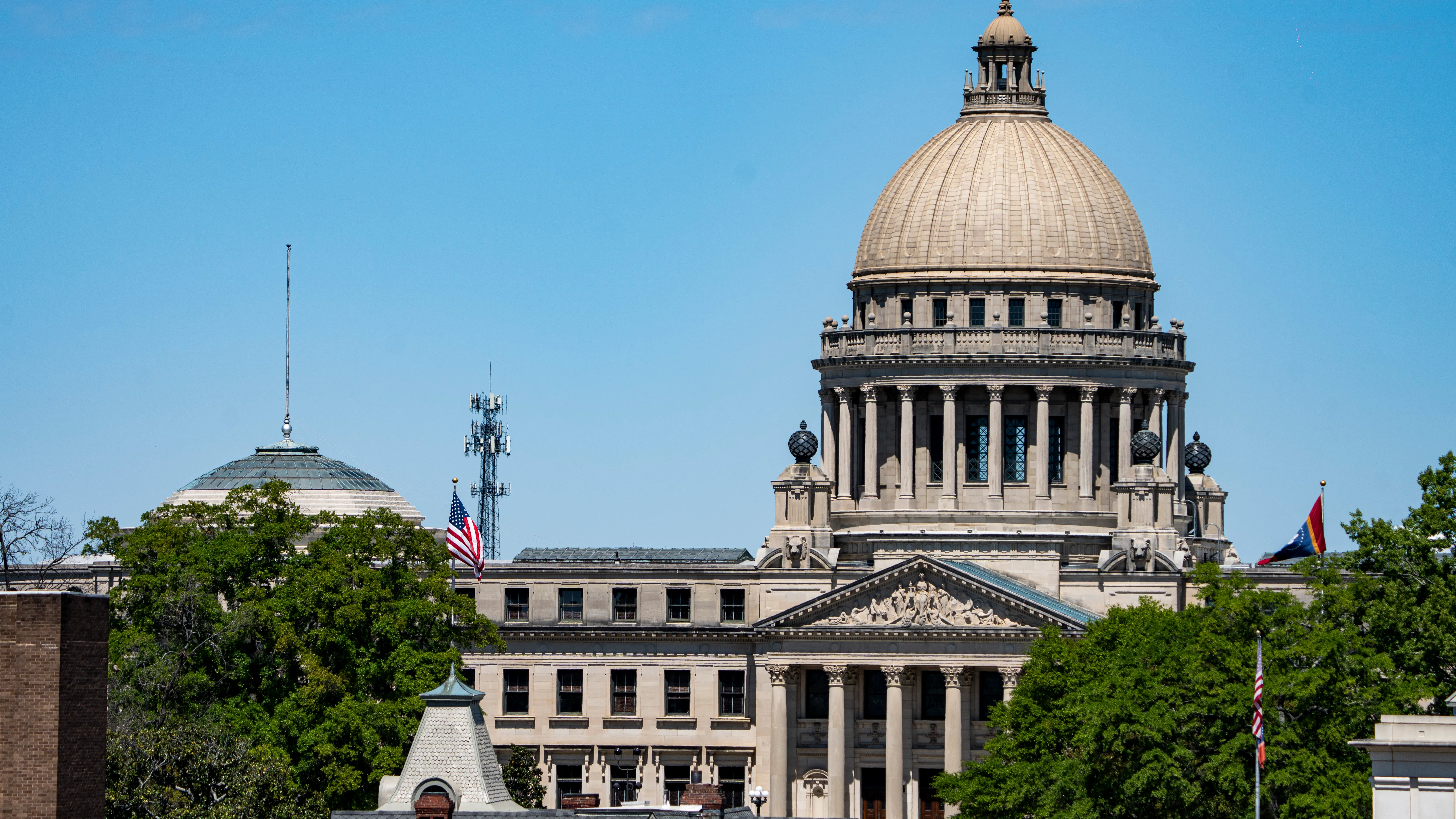 The Mississippi State Capitol building in Jackson with people walking near the entrance on a clear day, news photography style