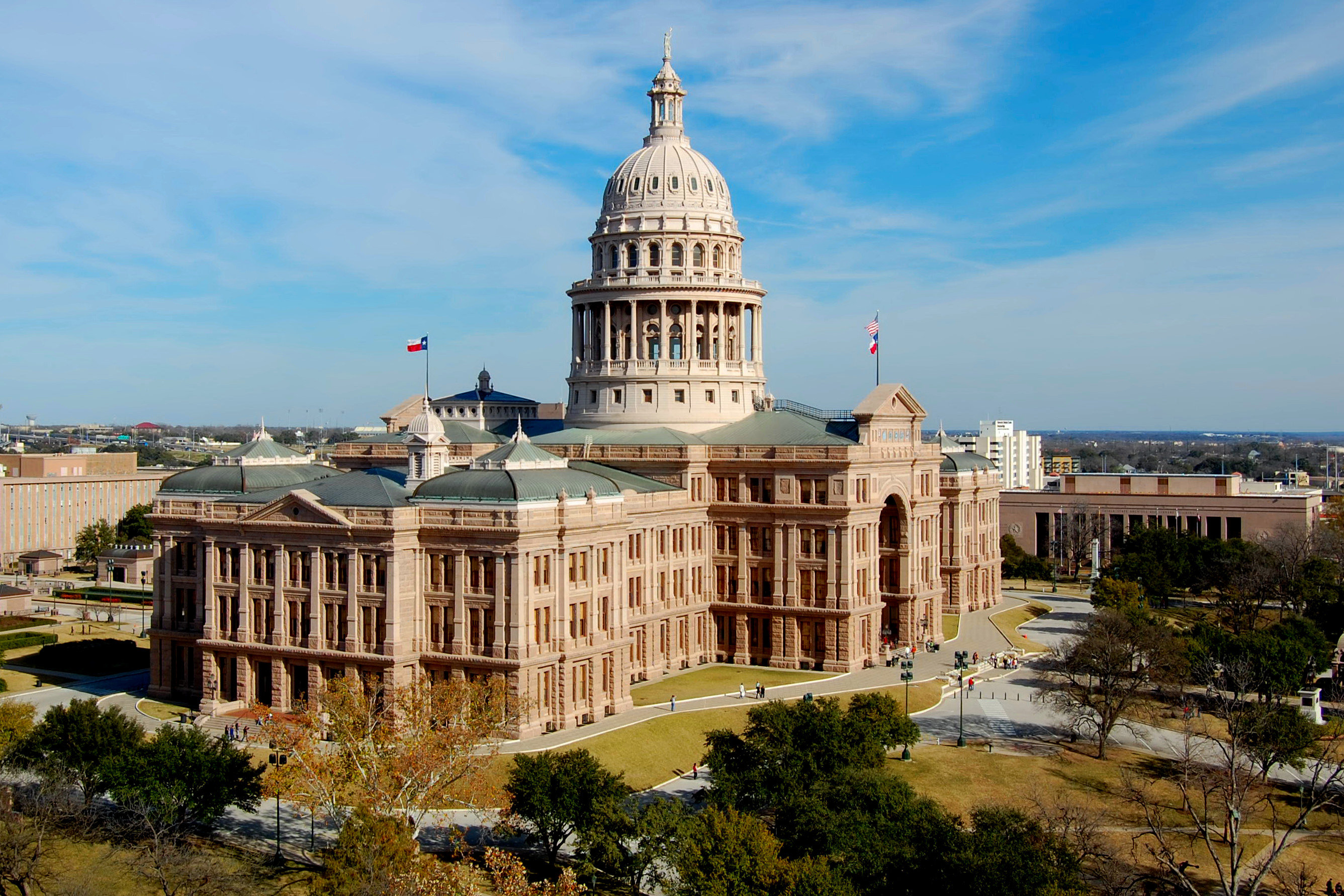 The Texas State Capitol building in Austin on a clear day, photographed from the lawn with people walking in the distance, news photography style