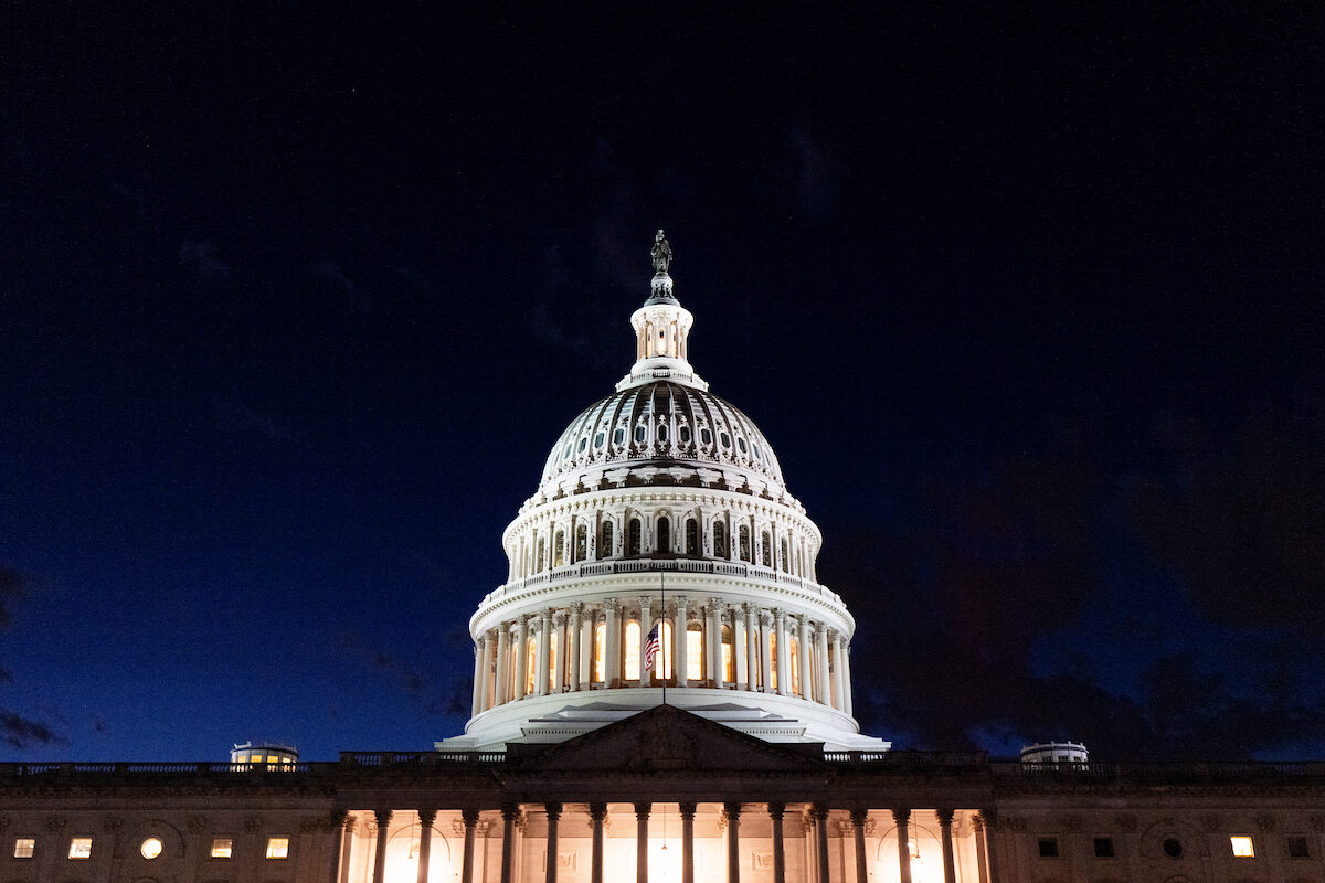 The U.S. Capitol building at dusk with lights on and a few people walking on the grounds, news photography style