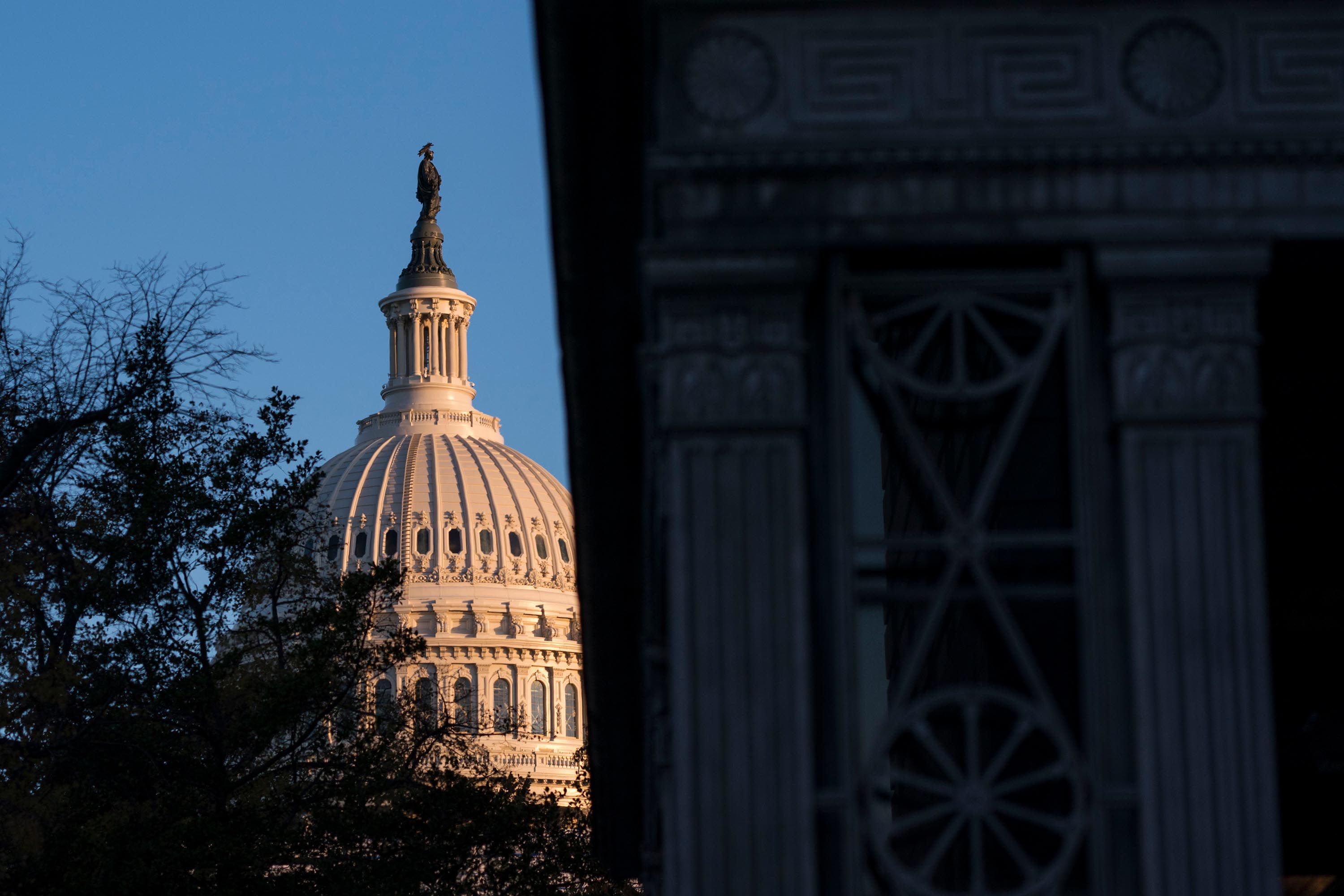 The United States Capitol building at dusk with lights glowing, photographed from the grounds in a realistic news photography style