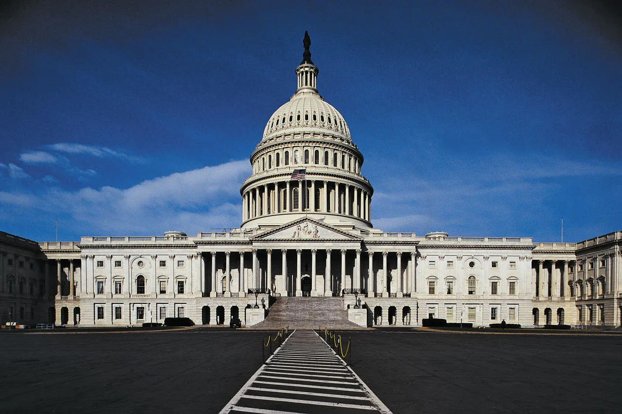 The United States Capitol building photographed from the National Mall on a clear winter morning, with the dome centered and people walking in the foreground, news photography style