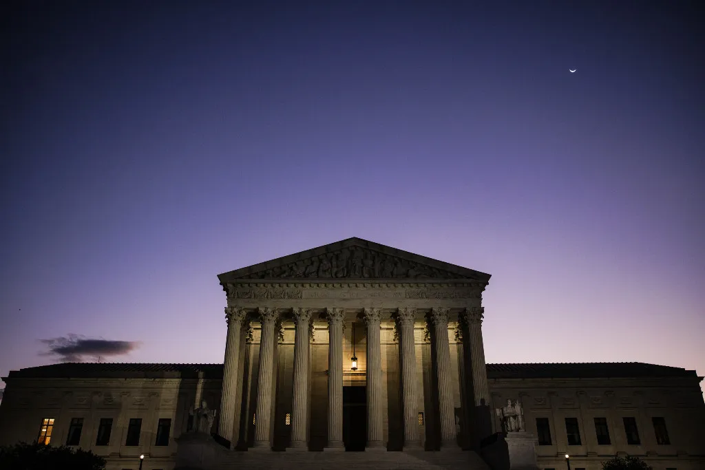 The United States Supreme Court building at dusk with the steps and columns lit by warm lights, news photography style