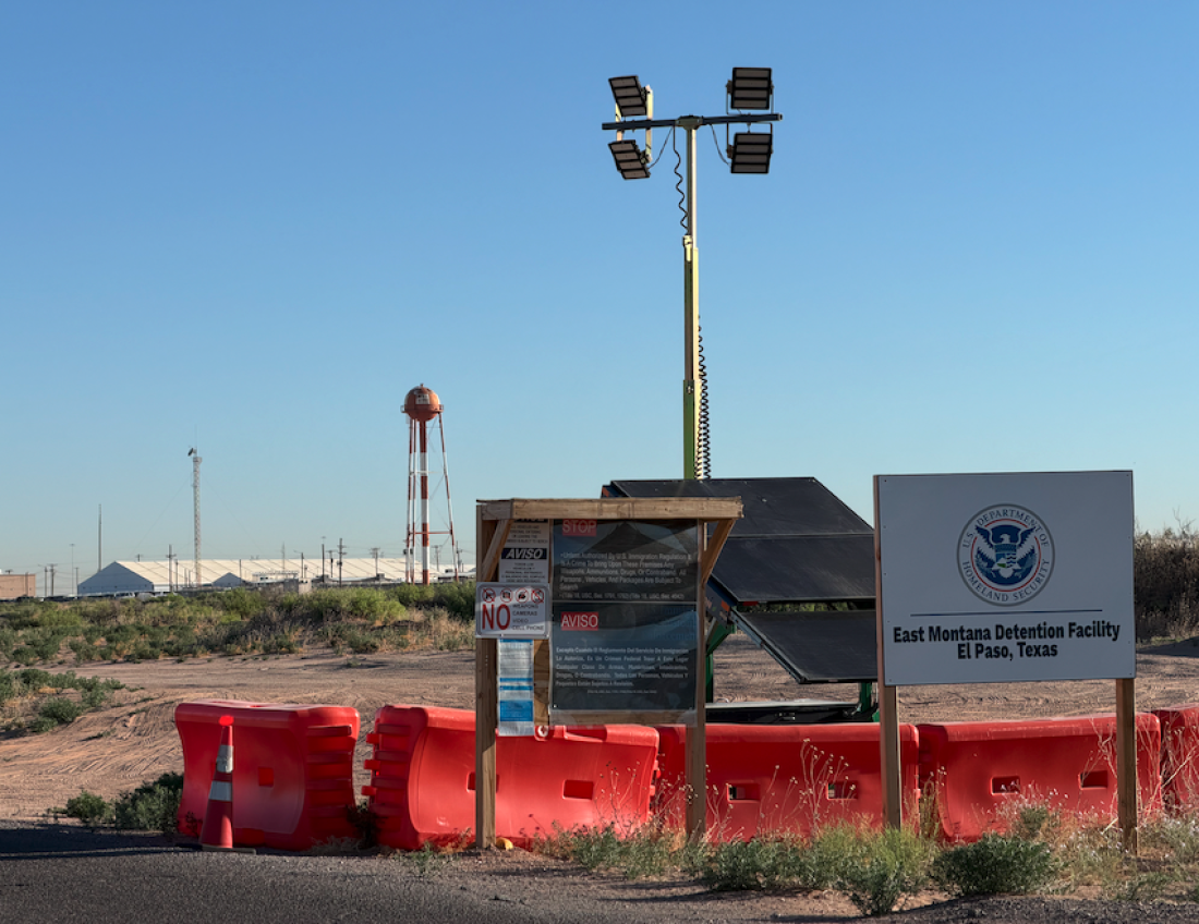 The entrance of an ICE detention facility in Texas with a secure gate and a sign near the driveway, photographed from a public roadside vantage point, news photography style