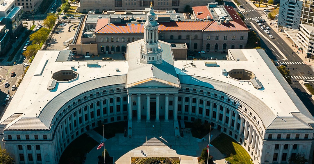 The entrance of the Denver City and County Building in downtown Denver on a clear day, with pedestrians walking past, news photography style