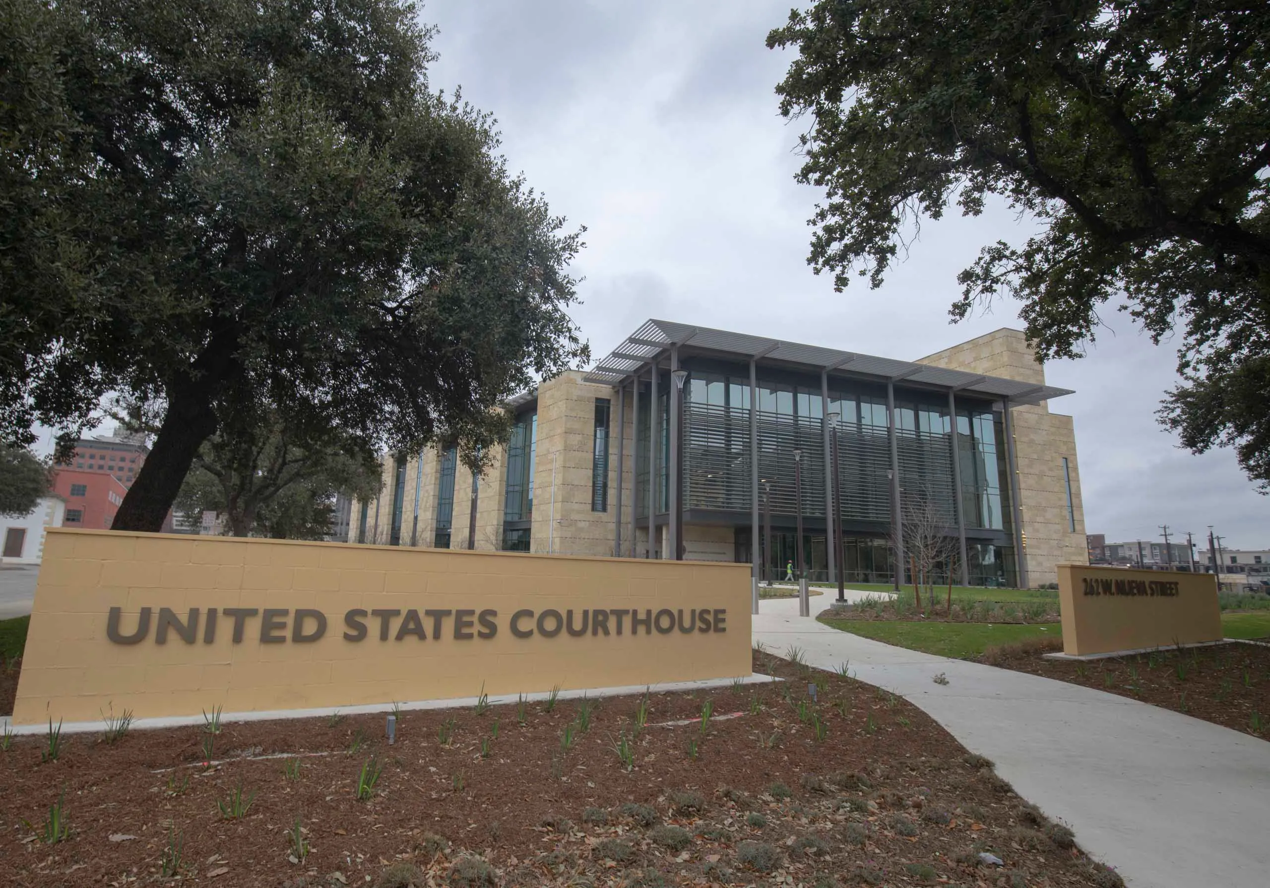 The exterior of a United States courthouse on a clear morning, with people walking up the courthouse steps, news photography style