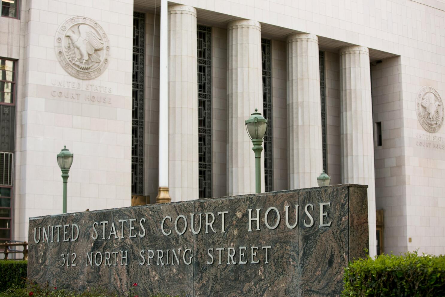 The exterior of a federal courthouse with stone steps and a U.S. flag flying on a pole, photographed in natural daylight, news photography style
