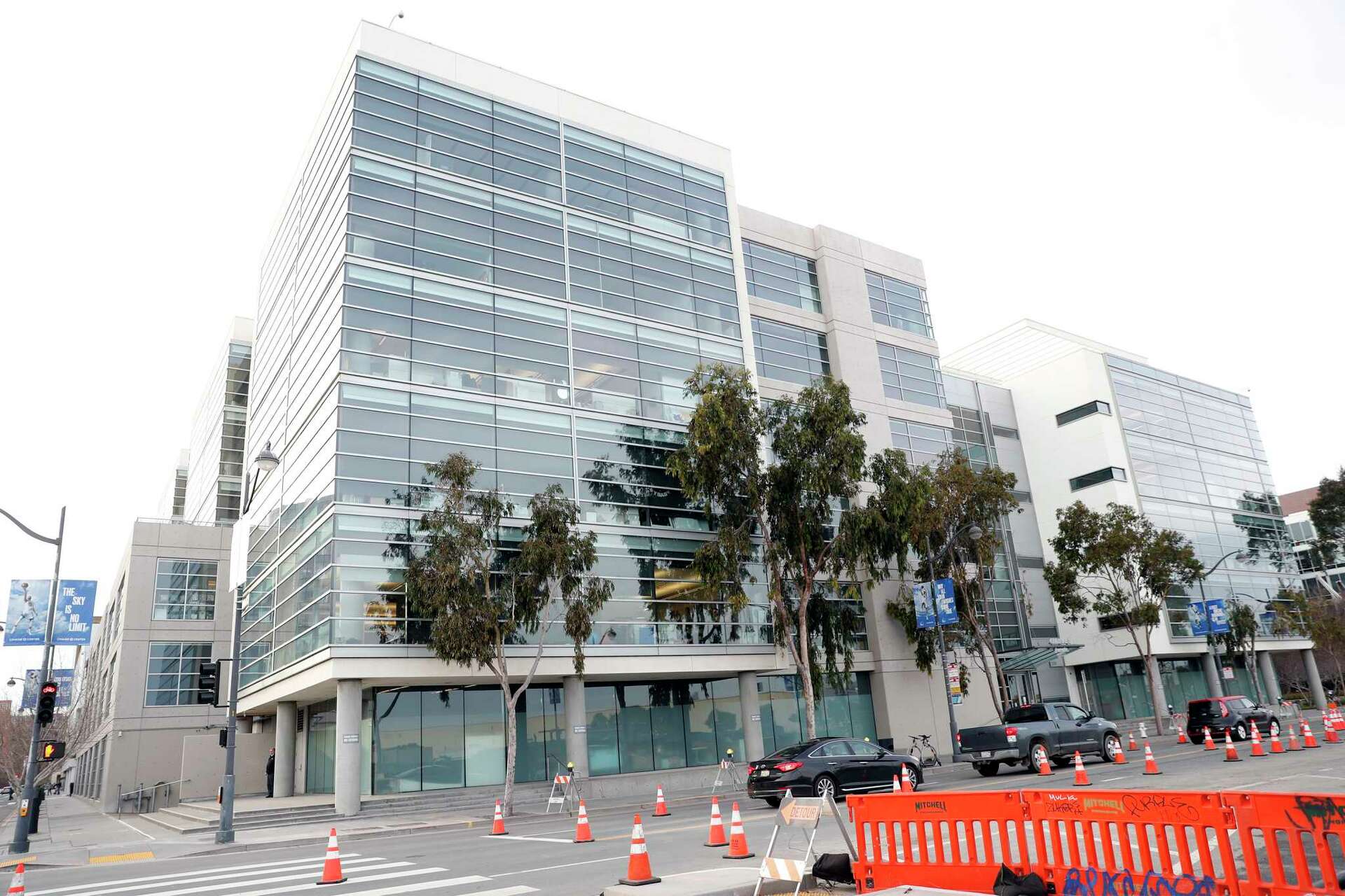 The exterior of an office building associated with OpenAI in San Francisco, with pedestrians walking past the entrance, news photography style