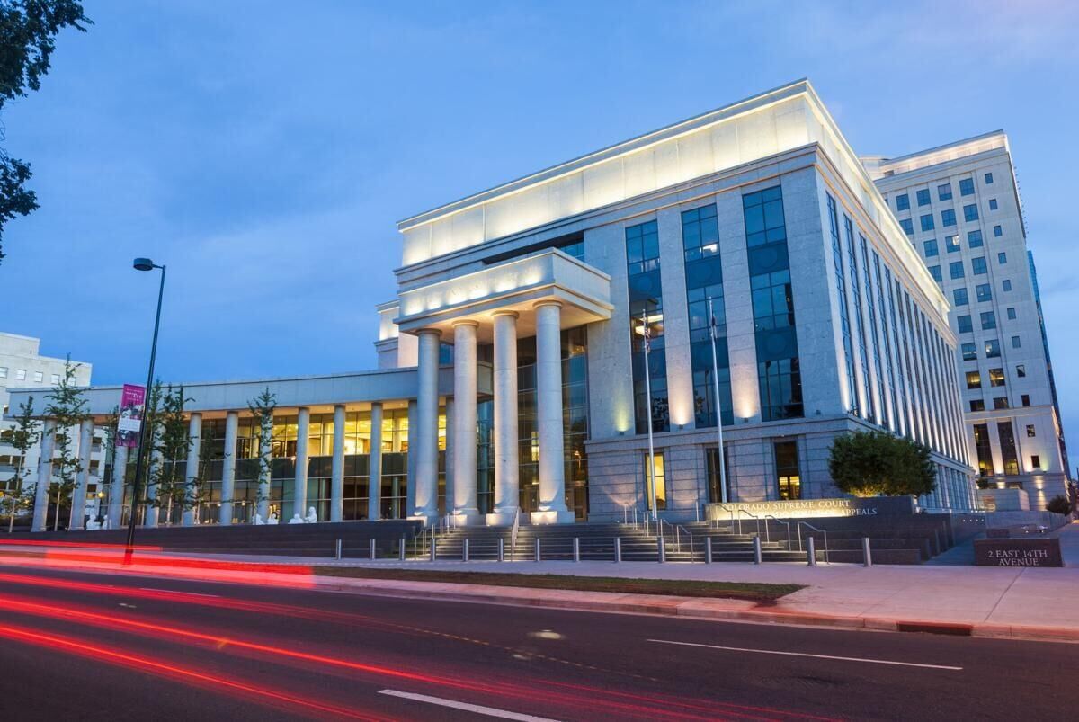 The exterior of the Colorado Supreme Court building in Denver on a clear day, with people walking nearby, realistic news photography style