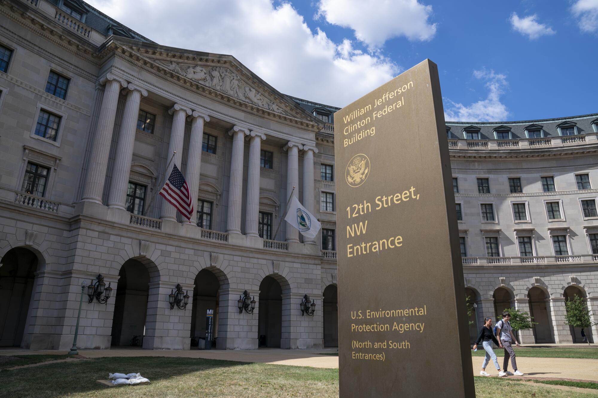The exterior of the Environmental Protection Agency headquarters in Washington, D.C. with pedestrians walking past on a clear day, realistic news photography style