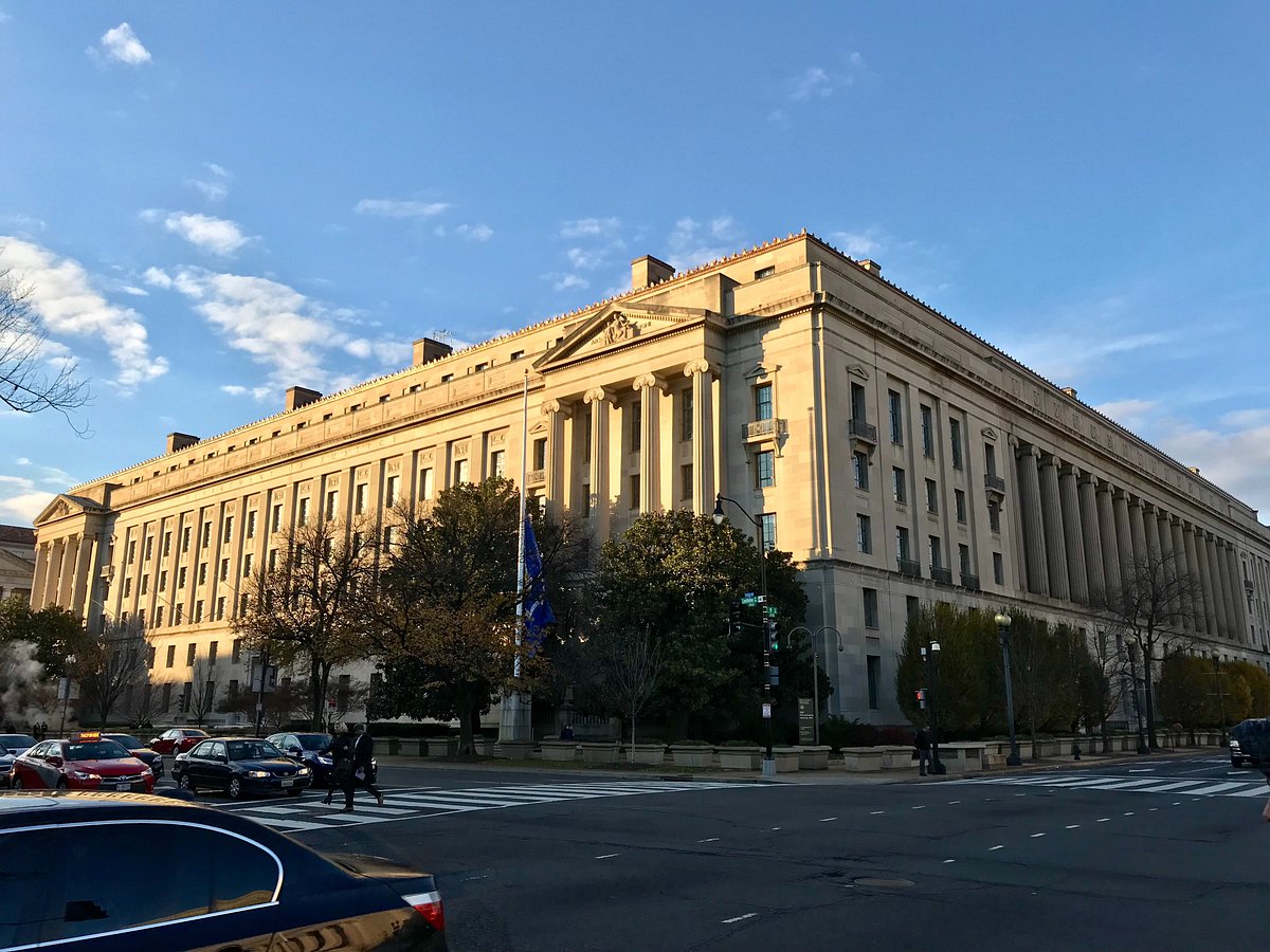 The exterior of the United States Department of Justice building in Washington, DC on a bright afternoon, straight-on news photography style