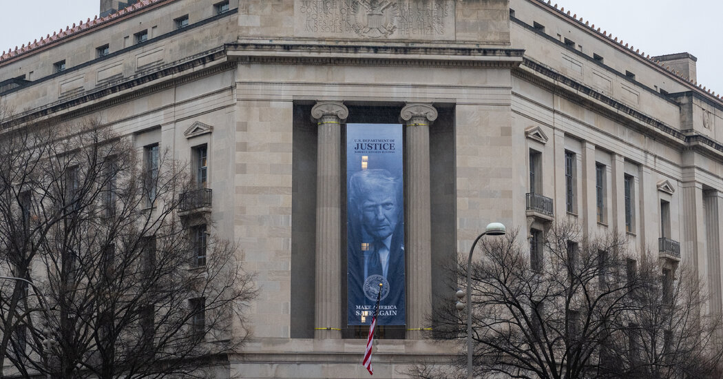 The exterior of the United States Department of Justice building in Washington, D.C., photographed on a clear day with pedestrians in the foreground, news photography style