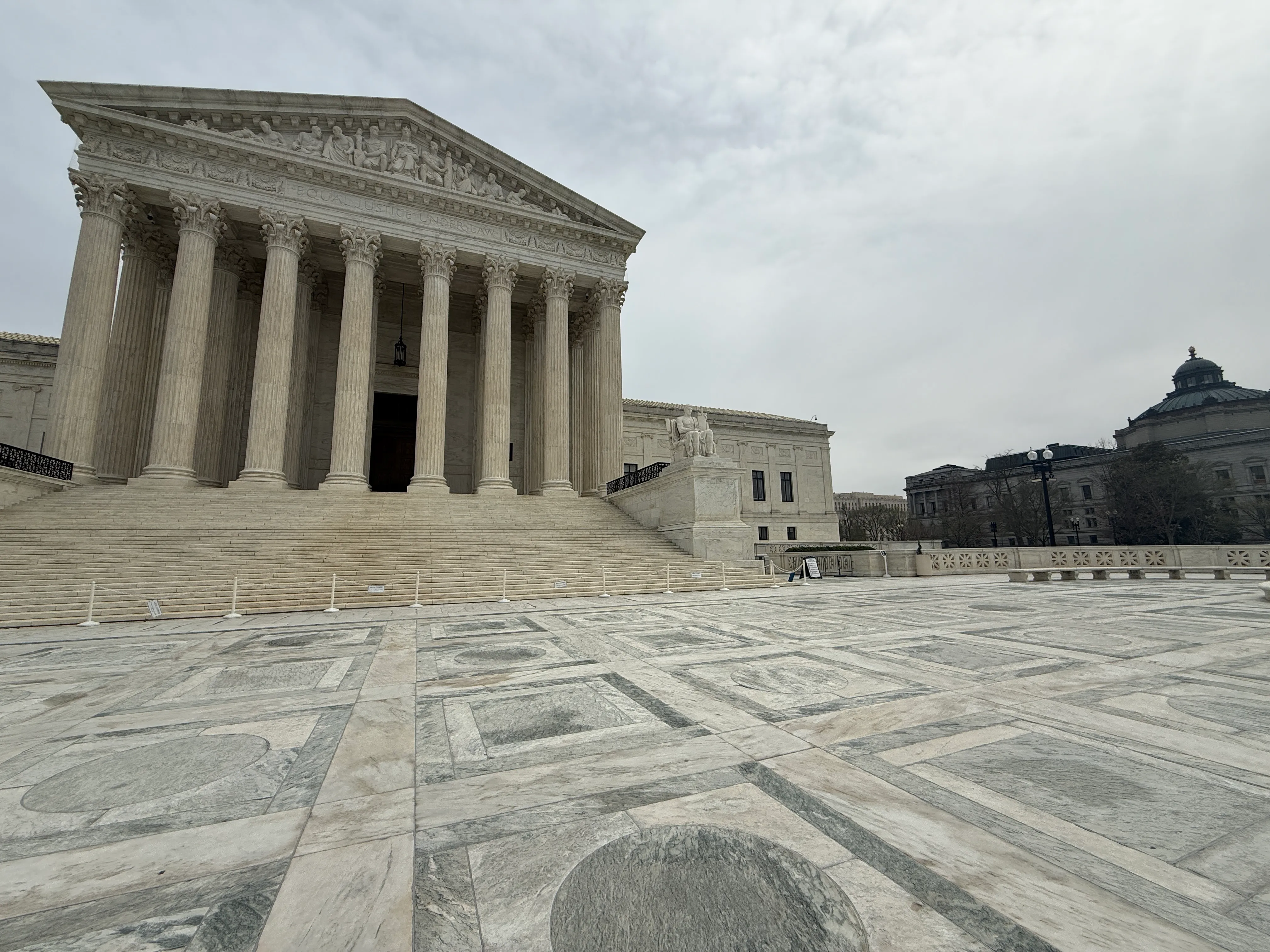 The exterior of the United States Supreme Court building in Washington, DC on a clear day, with people walking on the front steps, news photography style