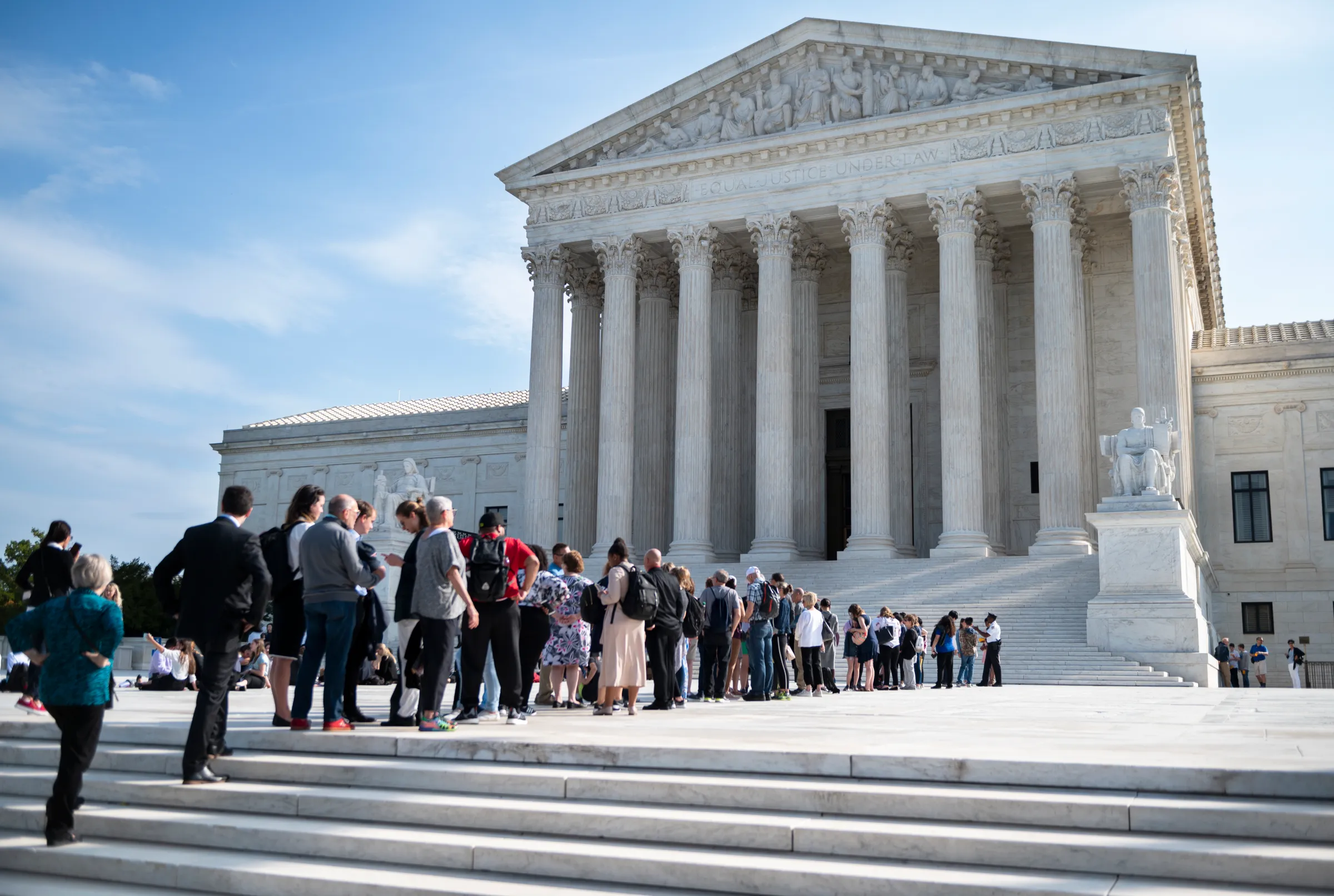 The exterior of the United States Supreme Court building in Washington, DC on a clear day, with the marble steps and columns visible, news photography style