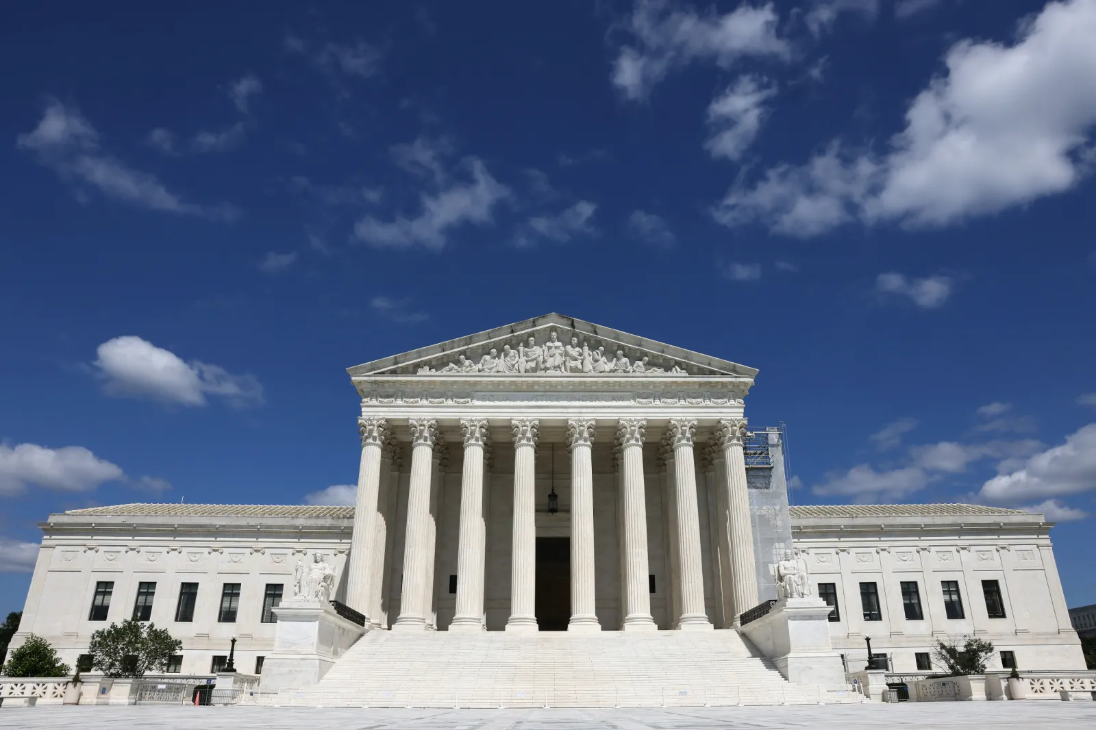 The exterior of the United States Supreme Court building in Washington, DC on a clear summer day, with the front steps and columns visible, news photography style