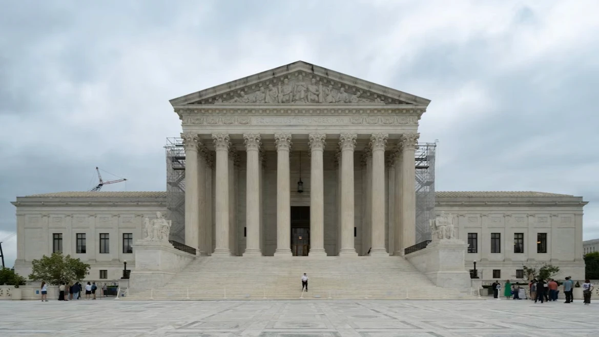 The exterior of the United States Supreme Court building on a clear day, with the front steps and columns visible, photographed from ground level, news photography style