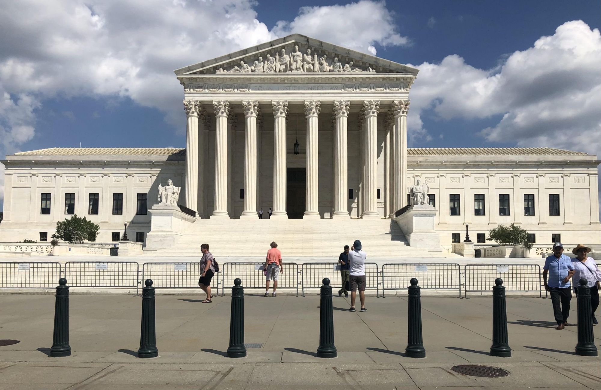 The exterior of the United States Supreme Court building in Washington, DC on a clear day with people walking on the steps, news photography style