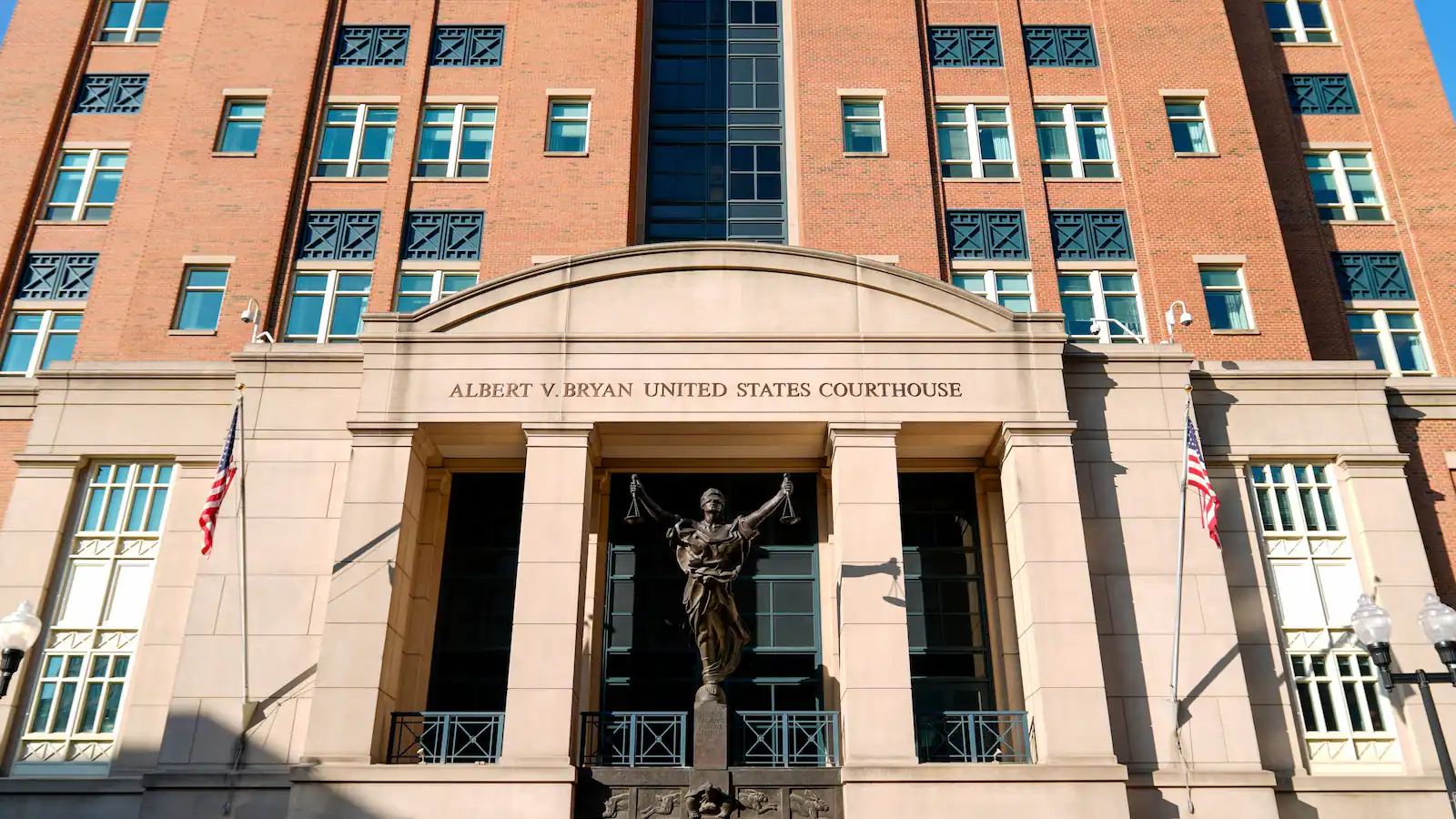 The exterior of the federal courthouse building in Alexandria, Virginia, photographed on a clear day with pedestrians nearby, news photography style
