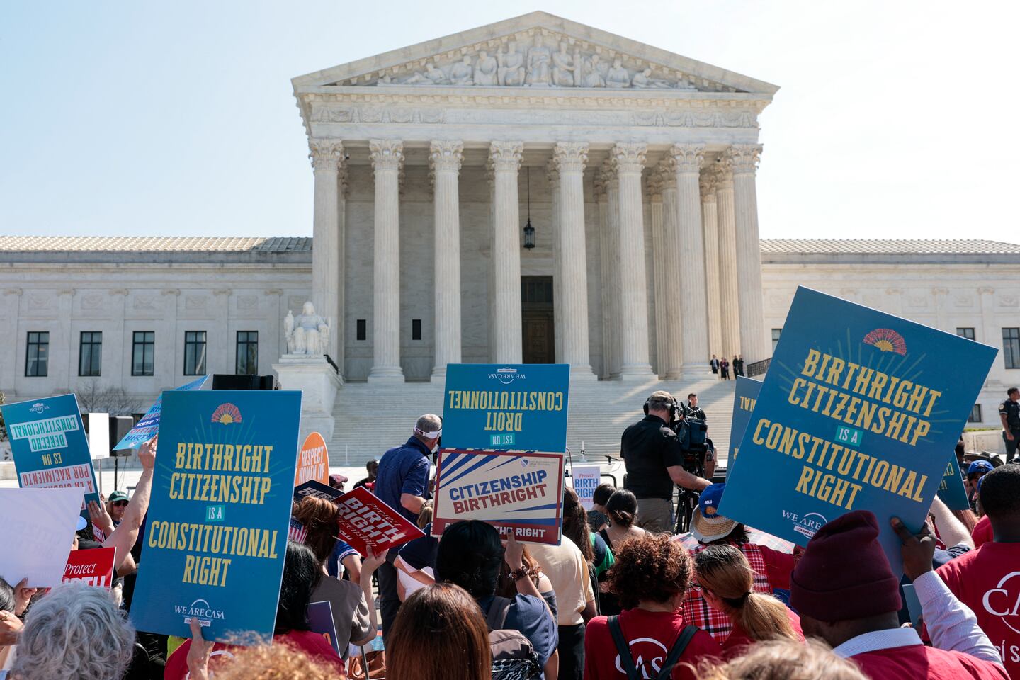 The exterior steps of the United States Supreme Court in Washington, D.C., with people gathered outside on a spring day, news photography style