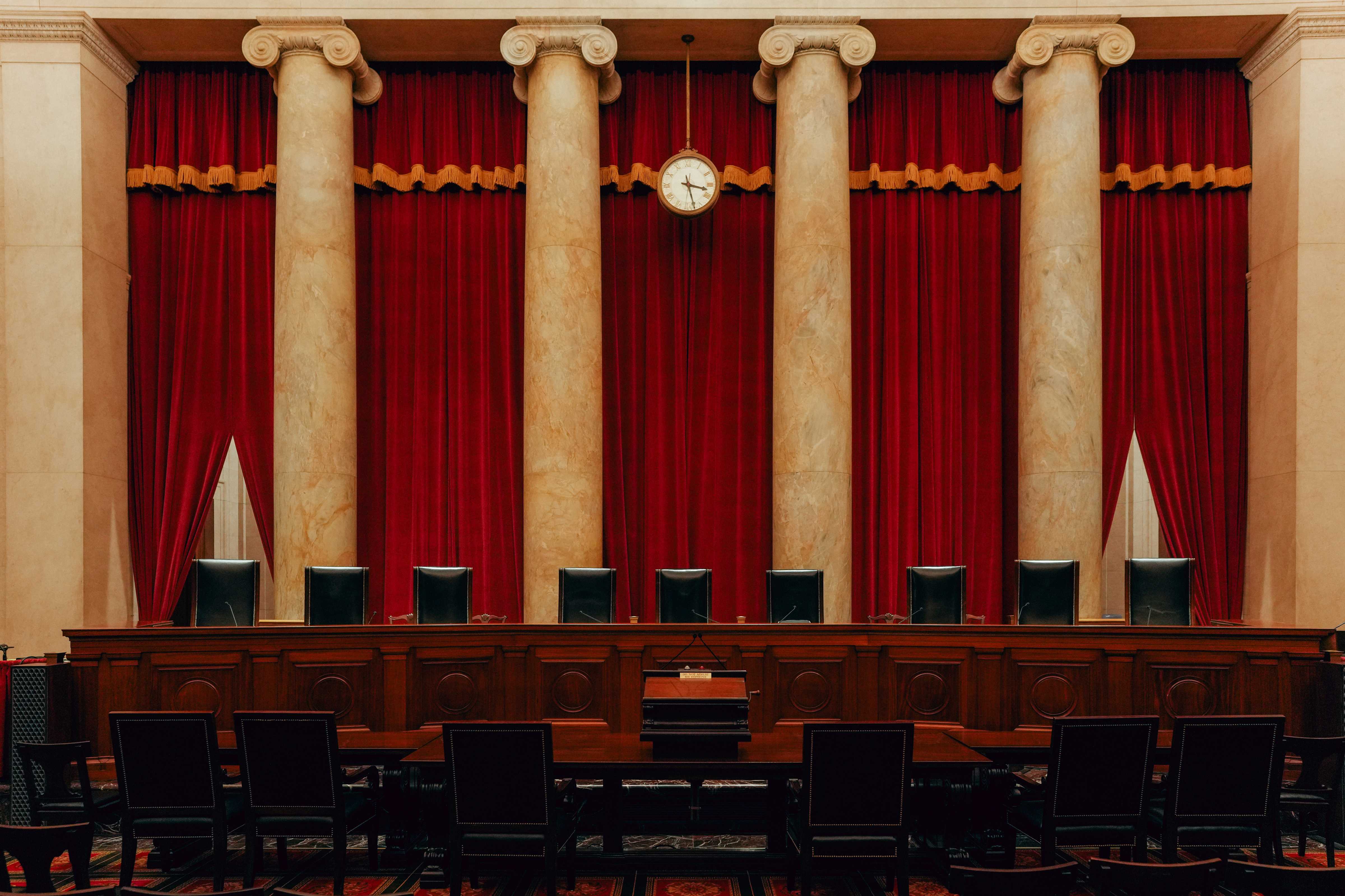 The interior of the United States Supreme Court courtroom with the bench, red drapery, and empty counsel tables, photographed from the public seating area
