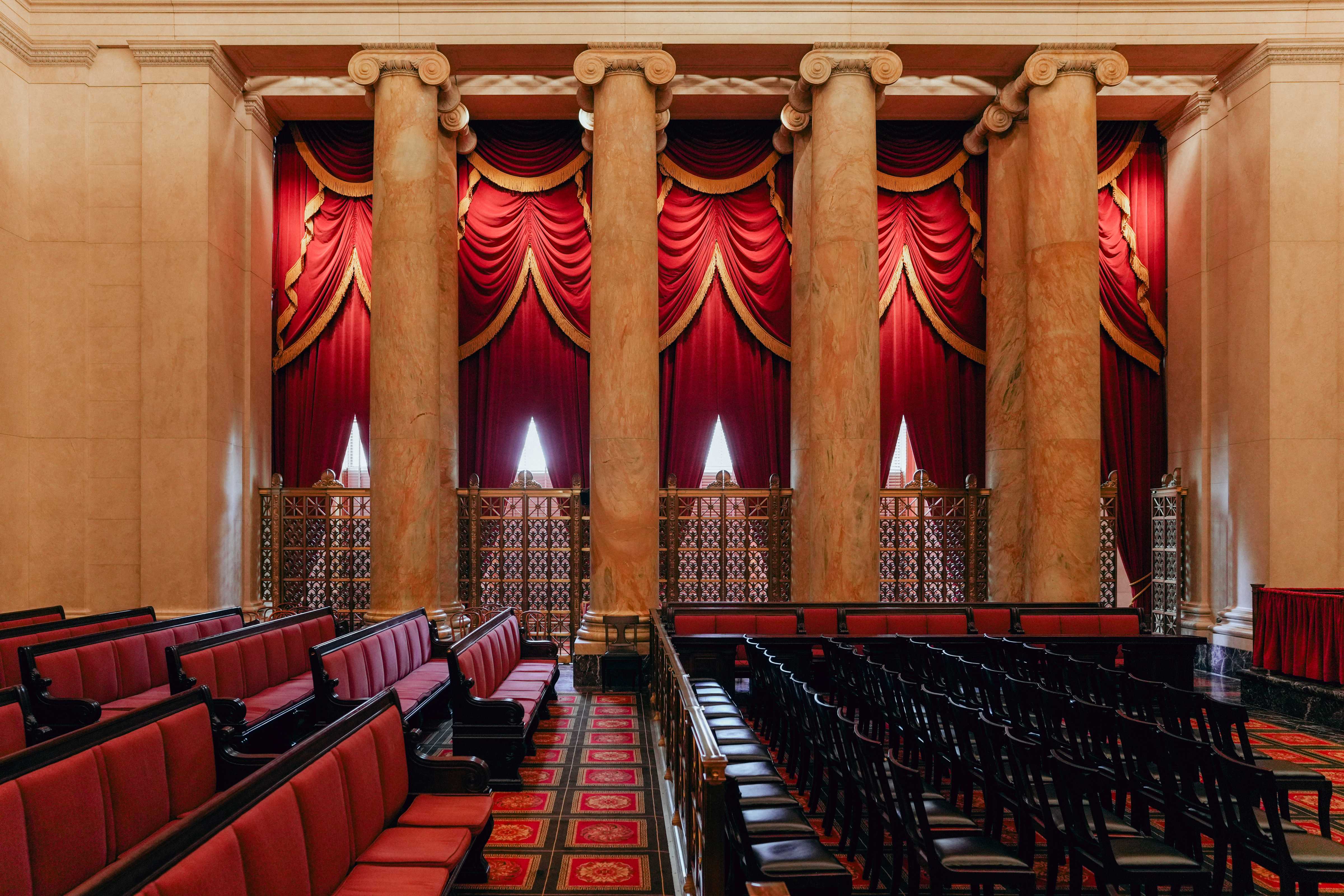 The interior of the United States Supreme Court courtroom with the bench, red drapes, and empty counsel tables in a quiet moment, news photography style