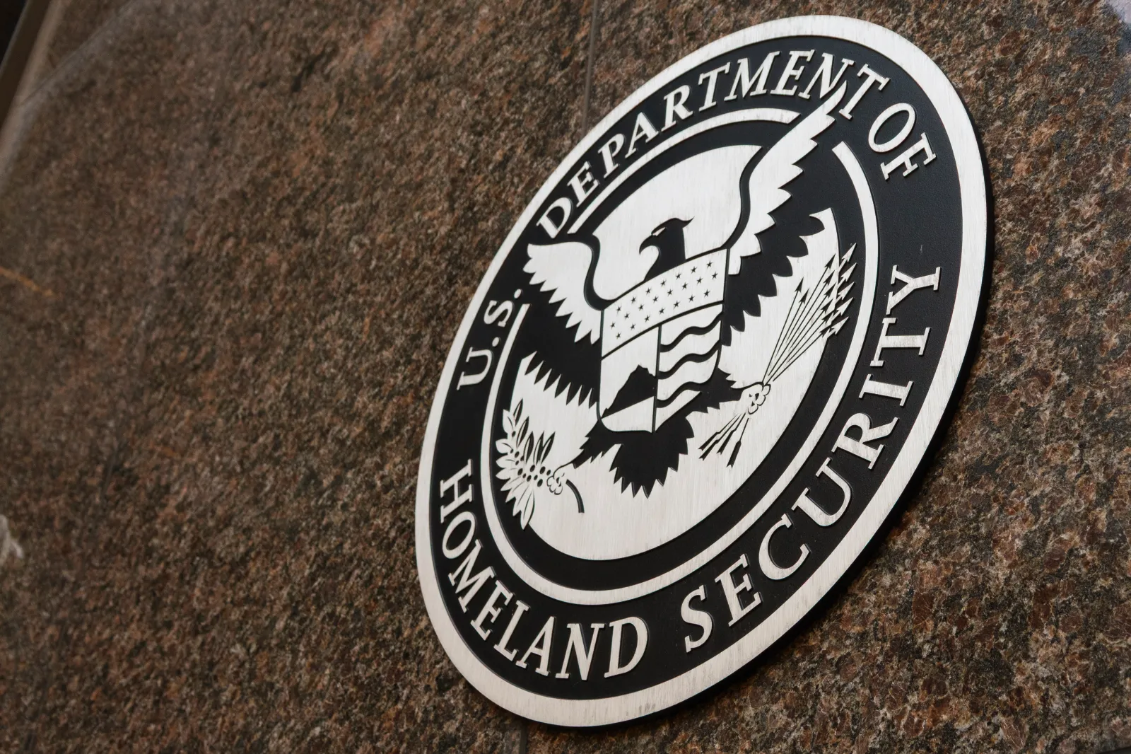 The seal of the U.S. Department of Homeland Security on a wall or podium, reflecting the federal authority that administers Temporary Protected Status.