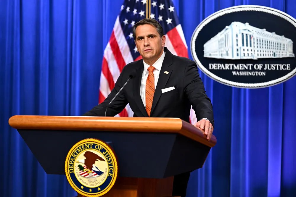 Todd Blanche standing at a Justice Department podium in Washington, D.C., speaking to reporters in an indoor press area, news photography style