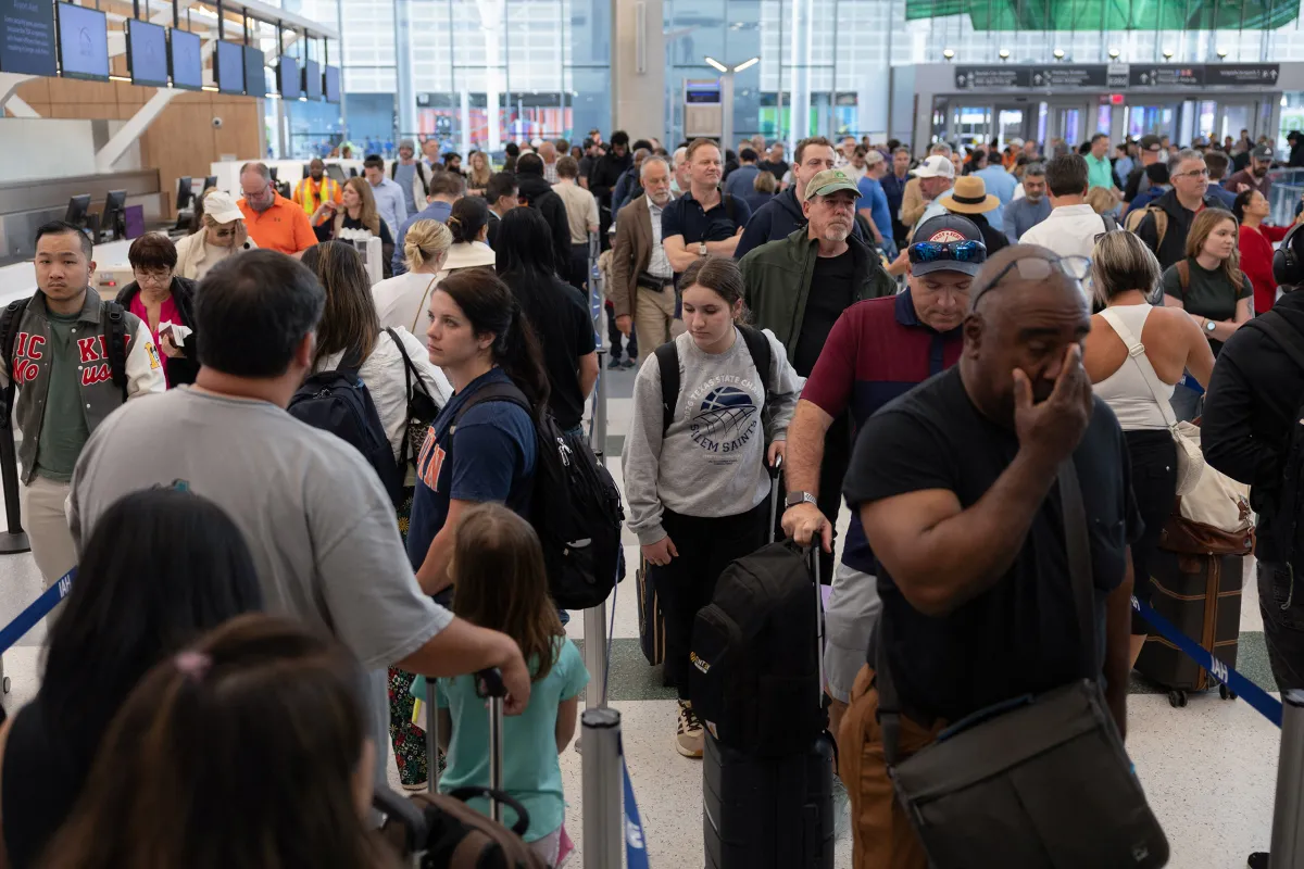 Travelers standing in a long TSA checkpoint line inside a busy airport terminal in Houston, with stanchions and security signage visible, news photography style