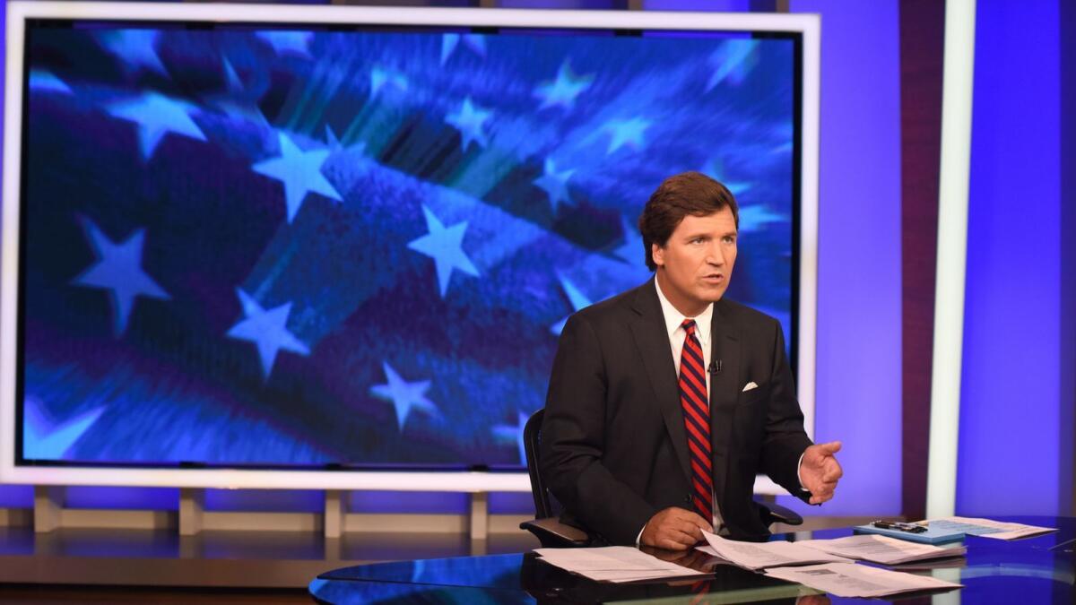 Tucker Carlson seated in a studio interview setting, facing an off-camera guest
