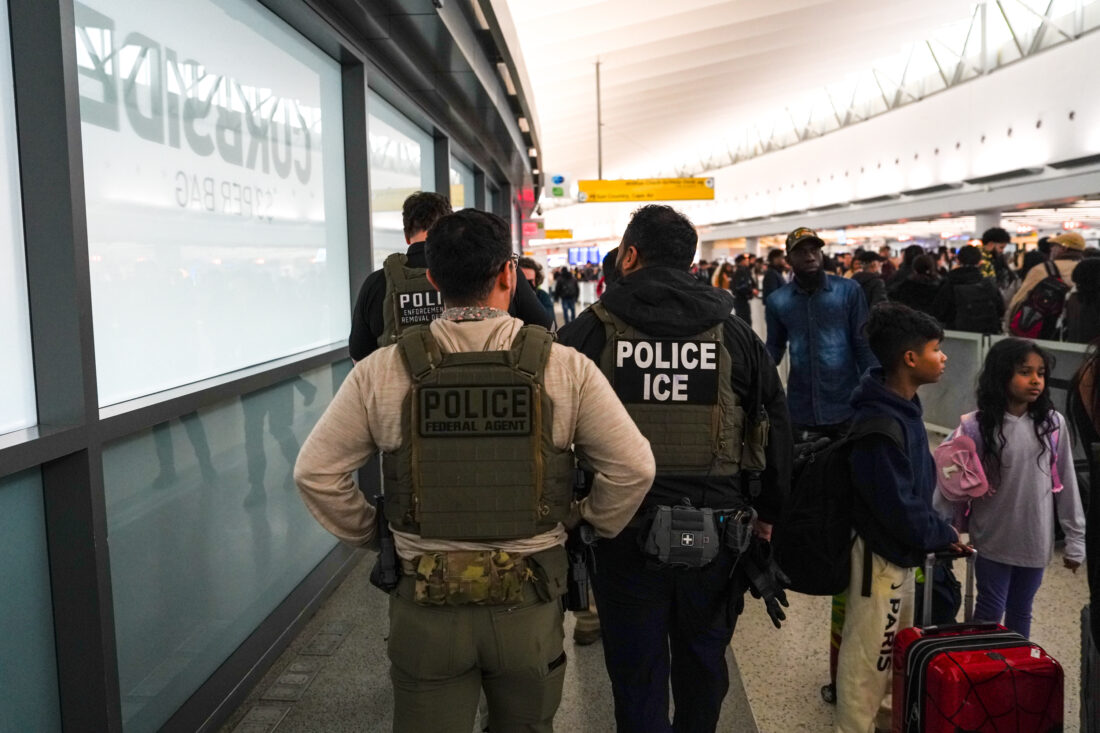 Two federal law enforcement agents in plain clothes walking past a government building entrance, photographed in a realistic news style