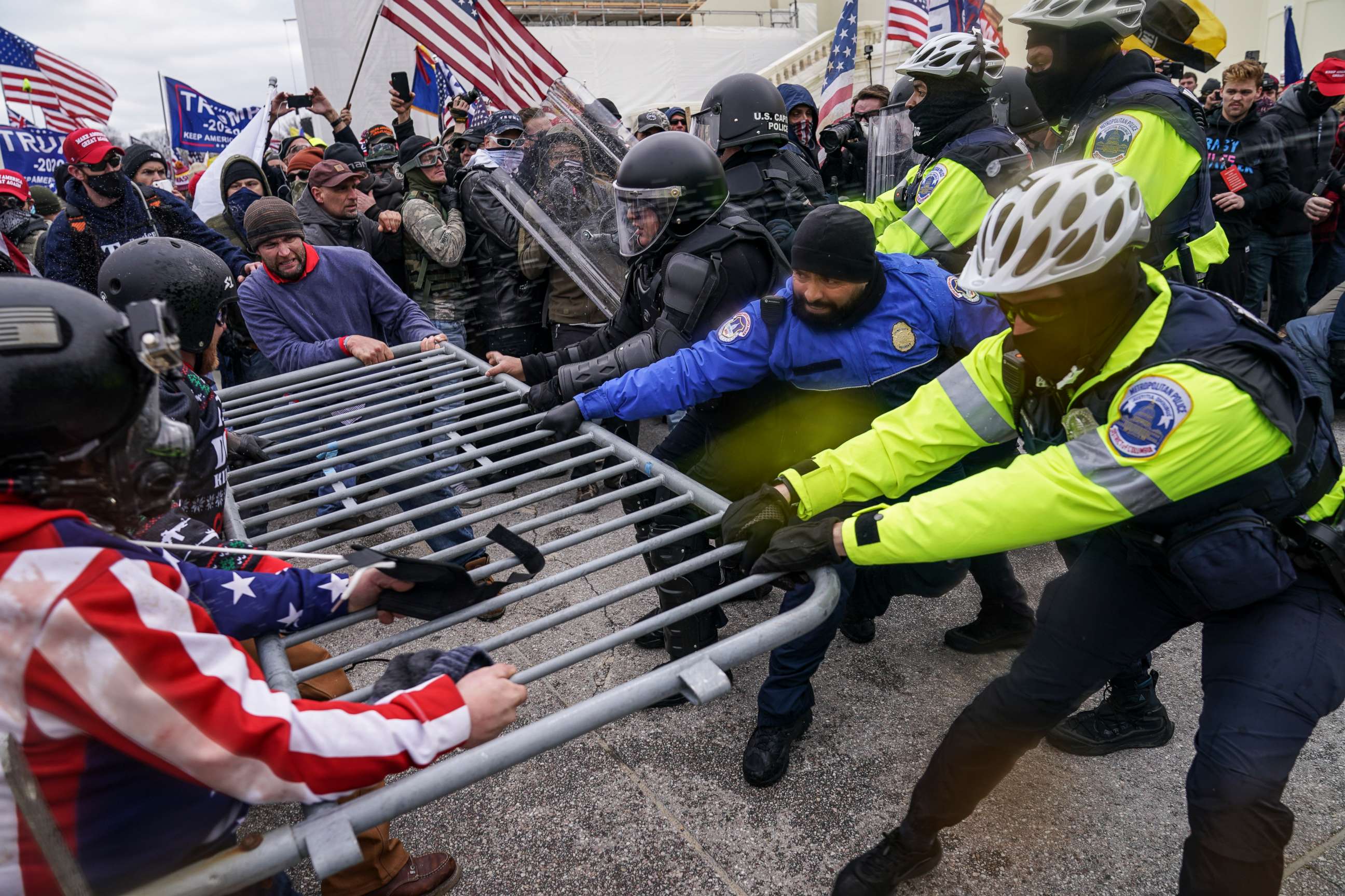 U.S. Capitol Police officers standing behind metal barricades near the Capitol grounds on a winter day, with the Capitol dome in the background, news photography style