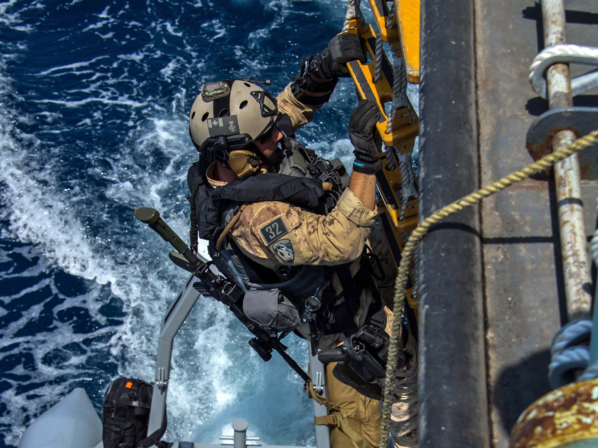 U.S. Navy sailors preparing for a boarding operation from a small boat alongside a larger vessel at sea, news photography style