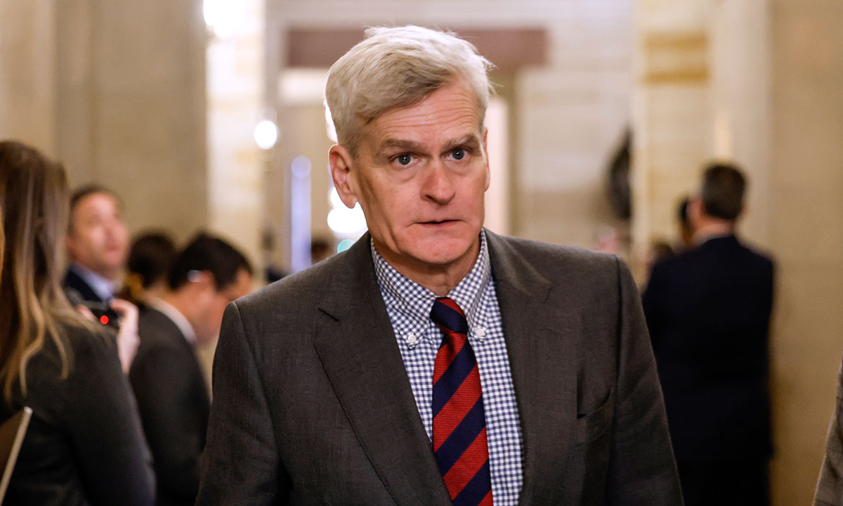U.S. Senator Bill Cassidy speaking to reporters in a Senate hallway, microphones extended toward him, candid news photo