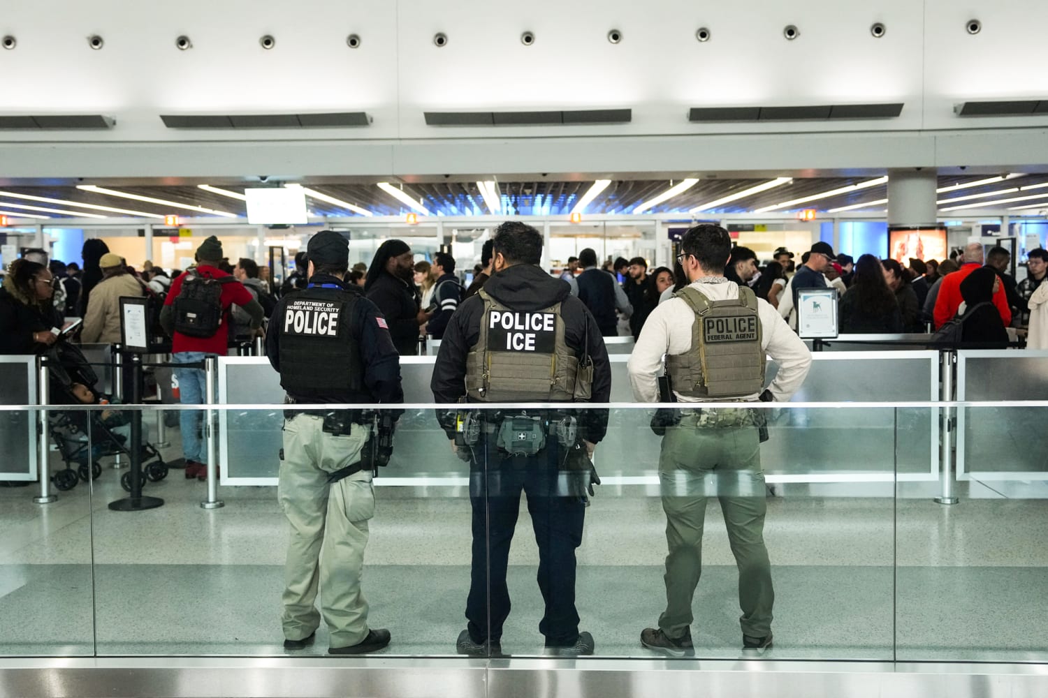 Uniformed federal agents walking through an airport terminal near a security area while travelers pull luggage in the background, photorealistic news photography