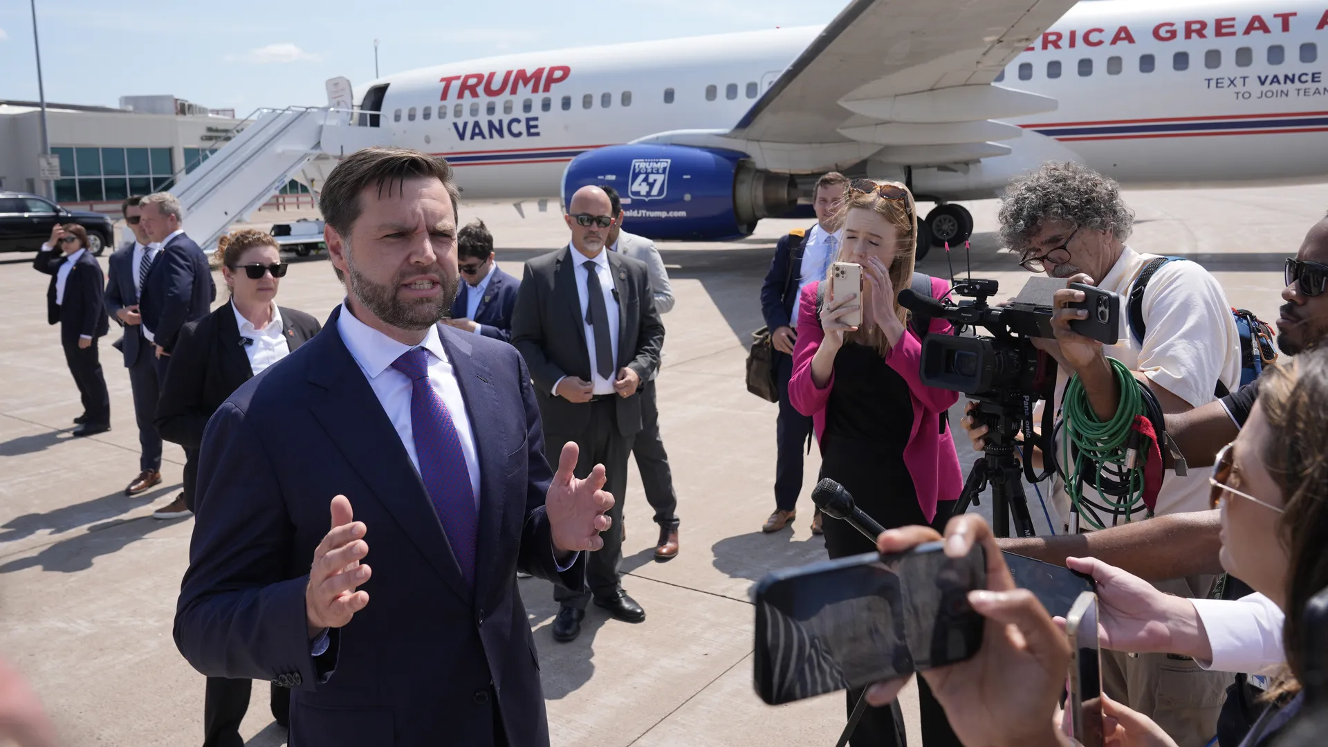 Vice President JD Vance speaking at the White House driveway press gaggle, standing near microphones with reporters gathered in front of him