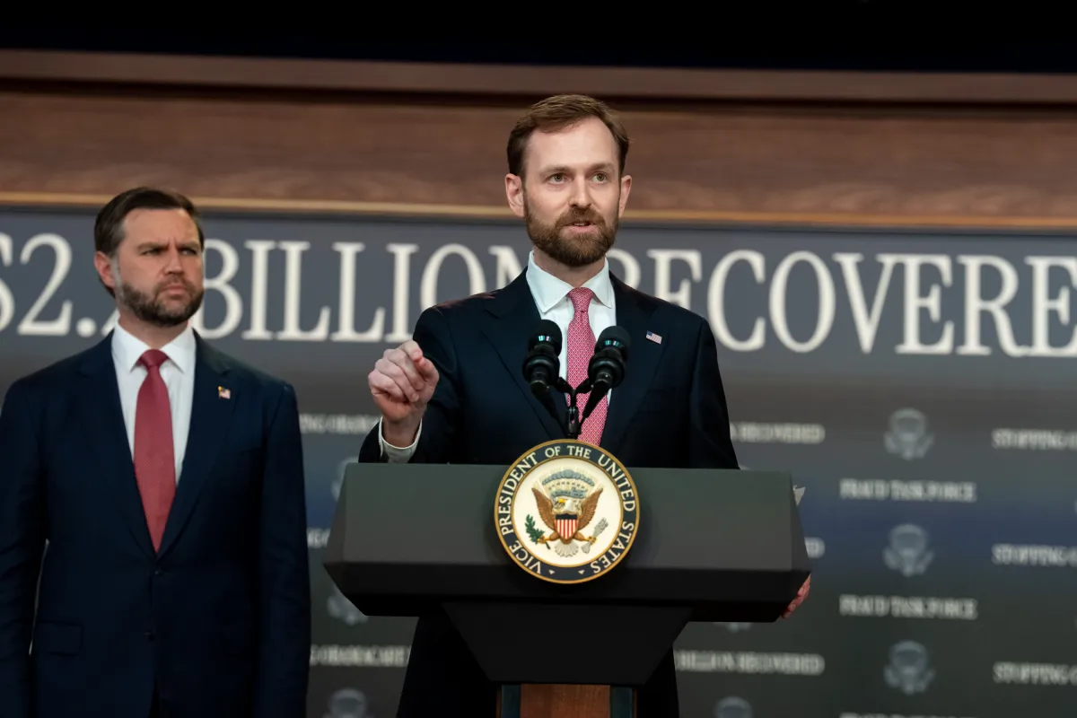 Vice President JD Vance speaks at a White House news conference podium as officials sit behind him.