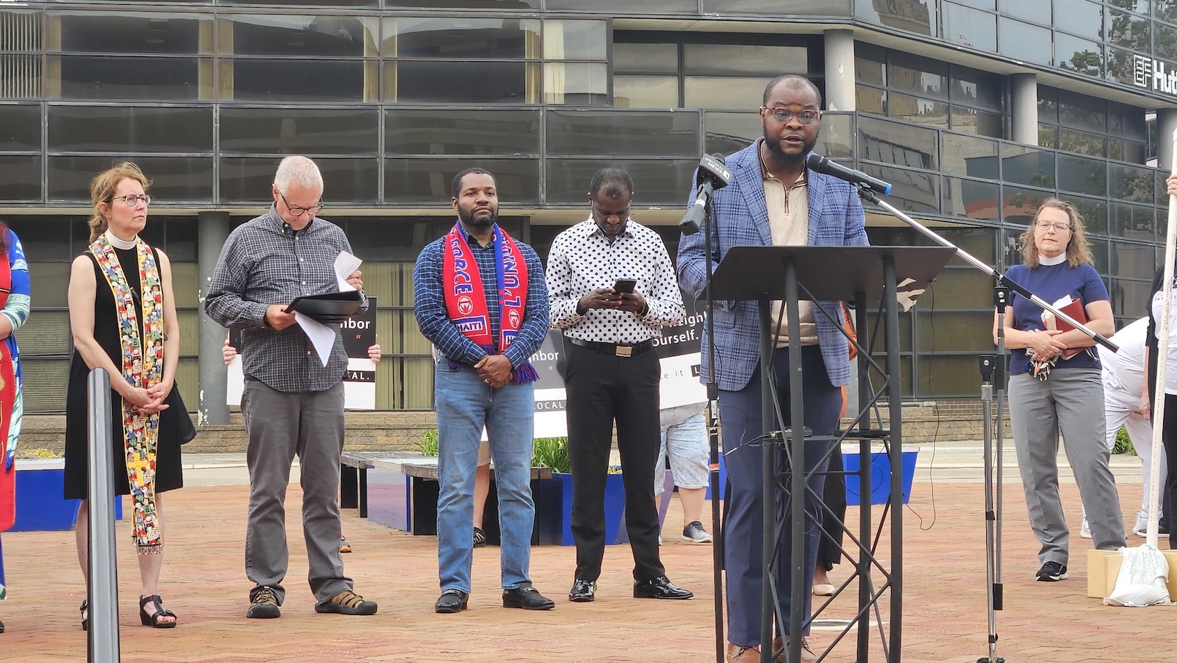 Viles Dorsainvil speaking at a community vigil in Springfield, Ohio, holding a microphone with attendees gathered behind him