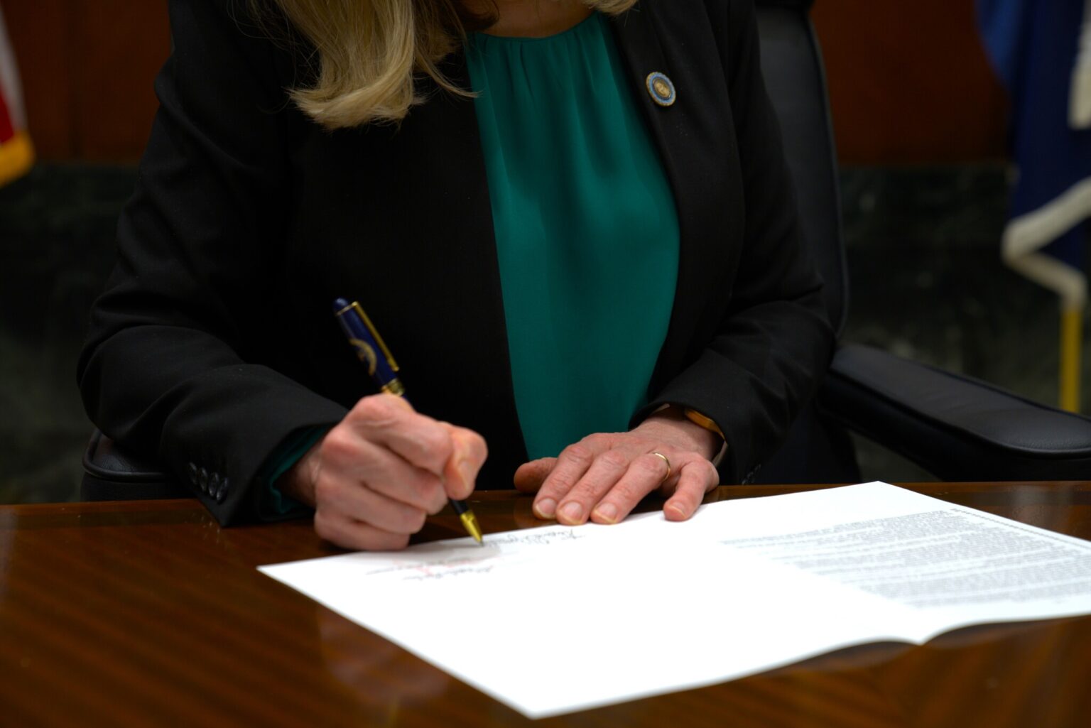 Virginia Governor Abigail Spanberger seated at a desk signing legislation with staff nearby, official event photography style