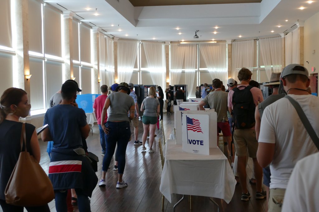 Voters standing in a line inside a public building polling place on election day, news photography style