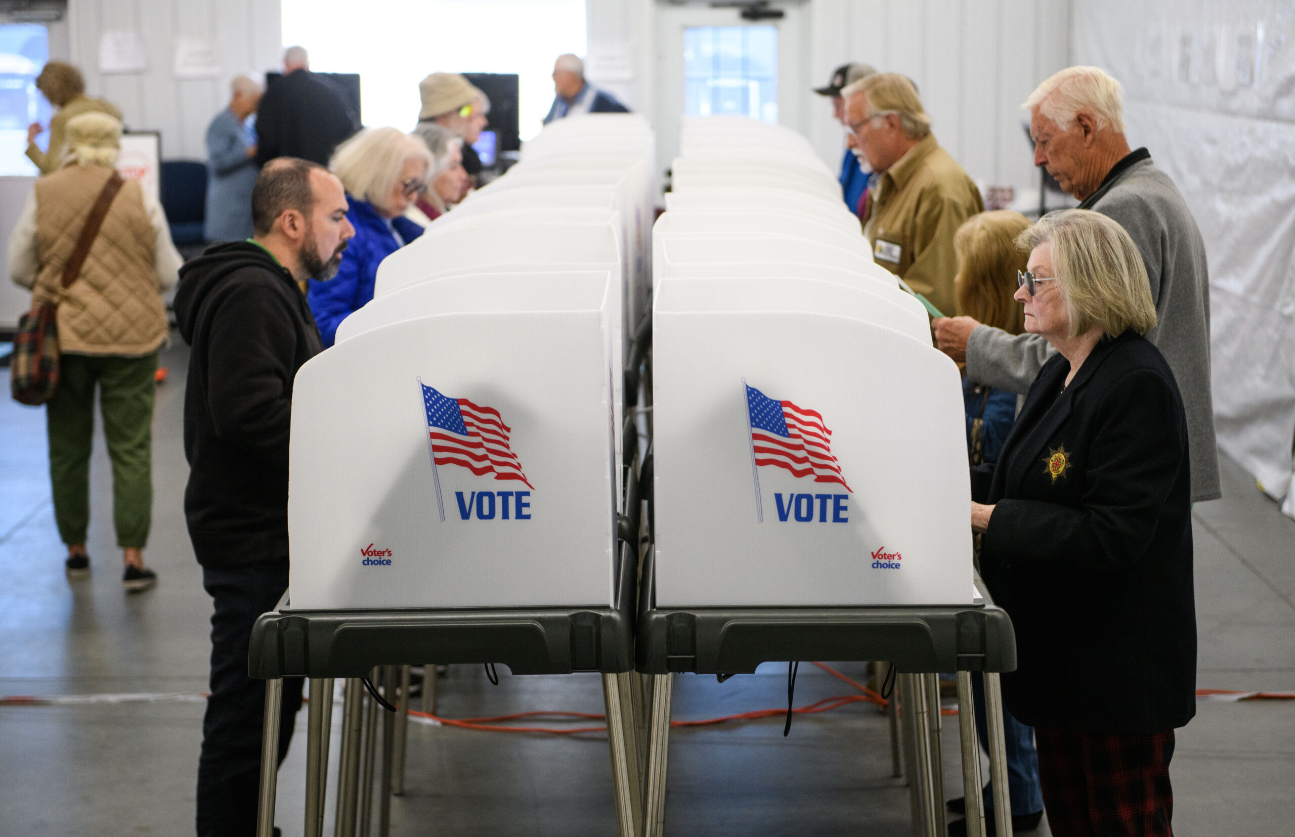 Voters standing in line inside a local polling place with election workers checking identification at a table, candid news photography style