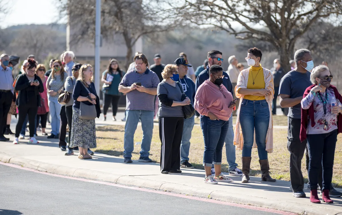 Voters standing in line outside a Texas polling location during a Texas primary election, with election workers near the entrance, news photography style
