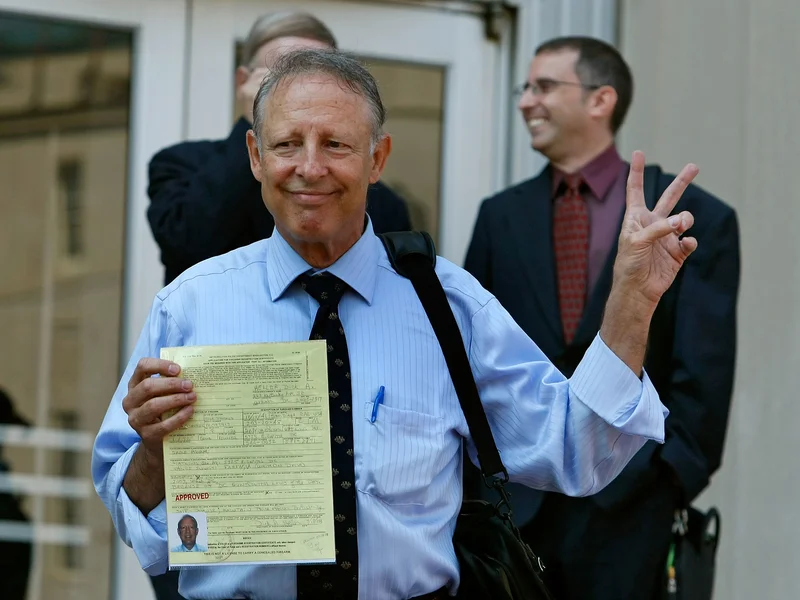 Dick Heller, plaintiff in the Supreme Court case District of Columbia v. Heller, gestures while holding his newly approved gun permit at the District of Columbia Police Department in August 2008,
