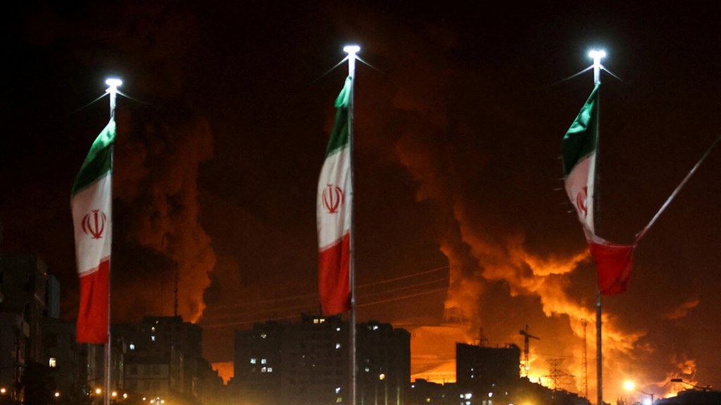 Iranian flags fly as fire and smoke from an Israeli attack on Sharan Oil depot rise, following Israeli strikes in Tehran on June 15, 2025. Majid Asgaripour/WANA/Reuters