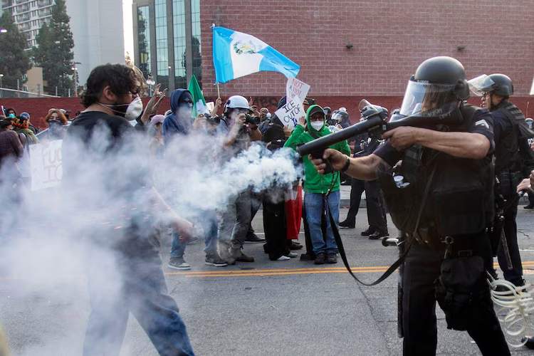 A police officer in riot gear fires a nonlethal weapon toward protesters during a demonstration following federal immigration operations in Los Angeles