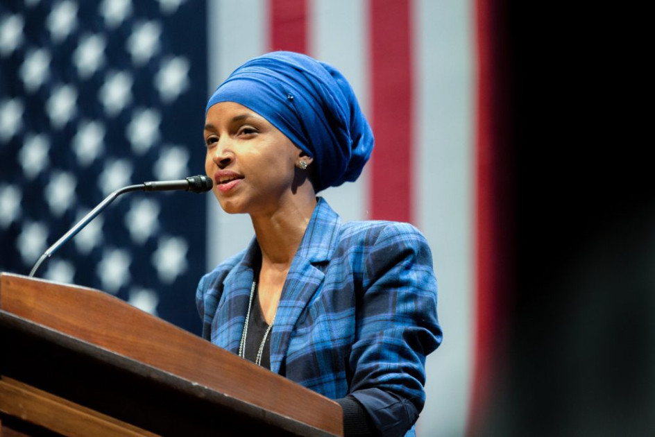 Ilhan Omar at a podium holding a pocket Constitution